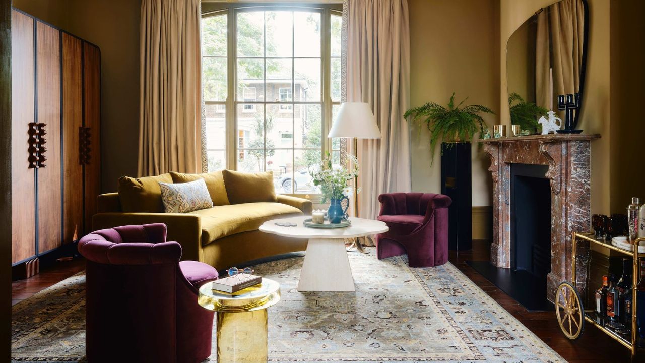 ochre painted grand living room with an antique red marble fireplace, a large window, yellow curved couch, round white coffee table, and purple curved arm chairs