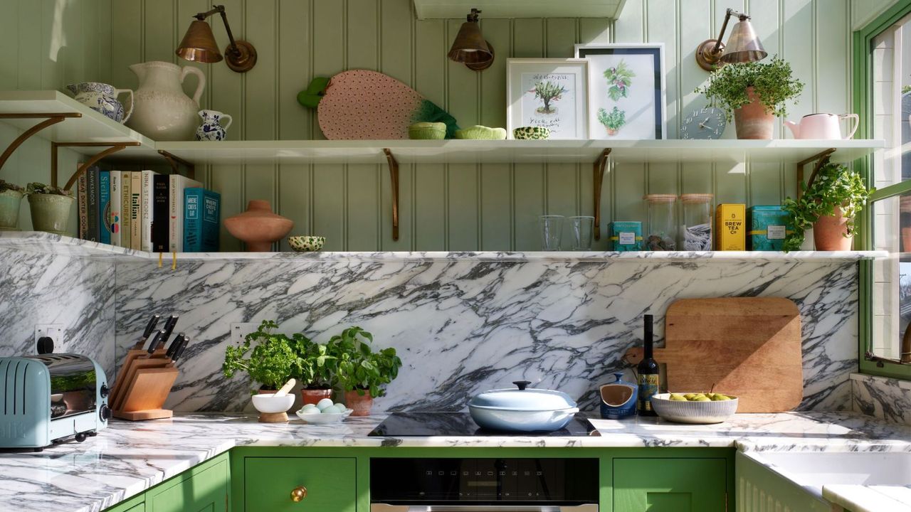 A green kitchen with marble countertops, paneled walls, and open shelving 