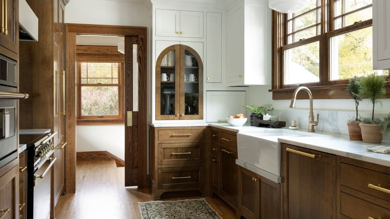 A wooden kitchen with white upper cabinets and brass hardware